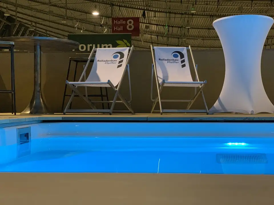 Beleuchteter Pool, dahinter Liegestühle mit Logo von Rollladenbau Pfeiffer