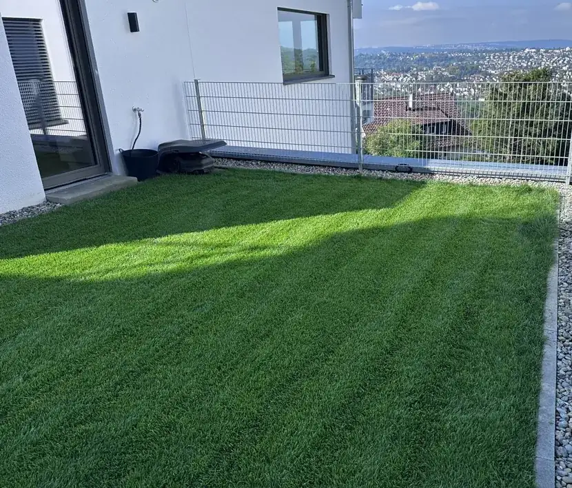 Frisch gemähter, dichter Rasen mit Streifen, dahinter Zaun und Aussicht über das Tal